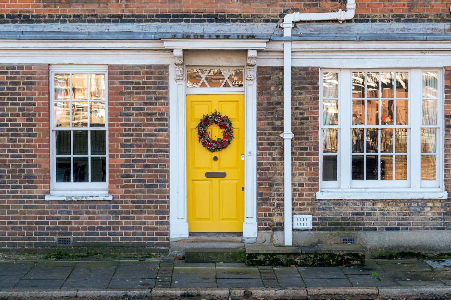 a yellow door with a wreath on it in front of a brick building